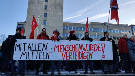 Foto mit einem Banner mit der Aufschrift Mit allen Mitteln: Menschenwürde verteidigen, gehalten von linken Genoss*innen und Sympathisant*innen