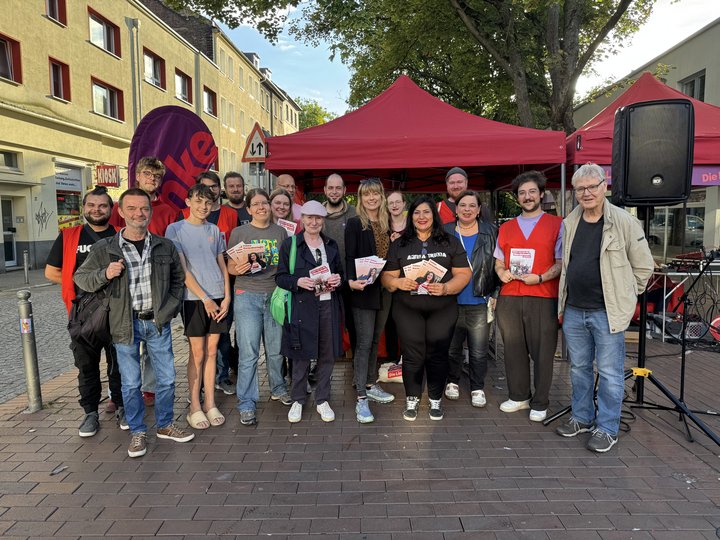 Eine größere Gruppe mit mehreren Personen steht mit Clara Bünger und Sonja Lemke, sowie Fatma Karacakurtoglu vor einem roten Pavillon