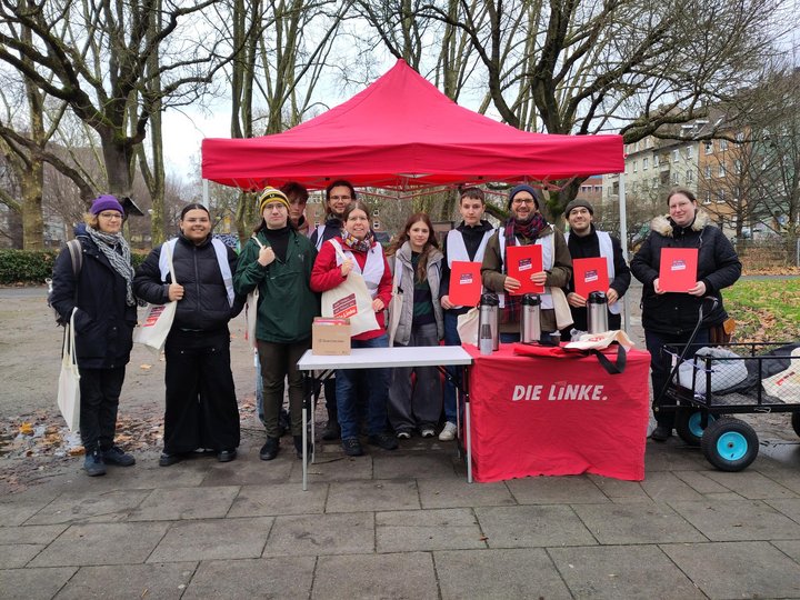 Ein Stand mit Pavillon von den Linken. Davor Linke Menschen ausgestattet mit Taschen, Westen und Klemmbretter