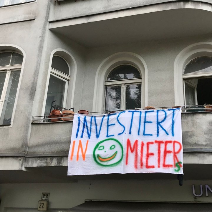 Eine Wohnung mit Balkon, worauf ein Banner mit dem Schriftzug "Investiert in Mieter" herunterhängt. 