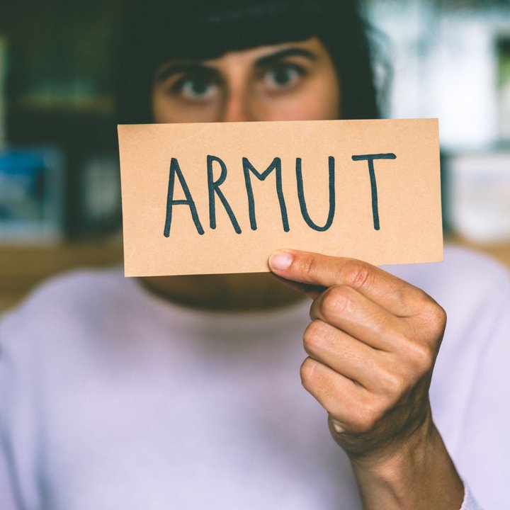 Das Bild einer Person, die ein Schild mit der Aufschrift Armut vor das Gesicht hält