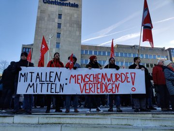 Foto mit einem Banner mit der Aufschrift Mit allen Mitteln: Menschenwürde verteidigen, gehalten von linken Genoss*innen und Sympathisant*innen