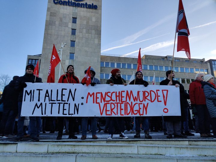 Foto mit einem Banner mit der Aufschrift Mit allen Mitteln: Menschenwürde verteidigen, gehalten von linken Genoss*innen und Sympathisant*innen