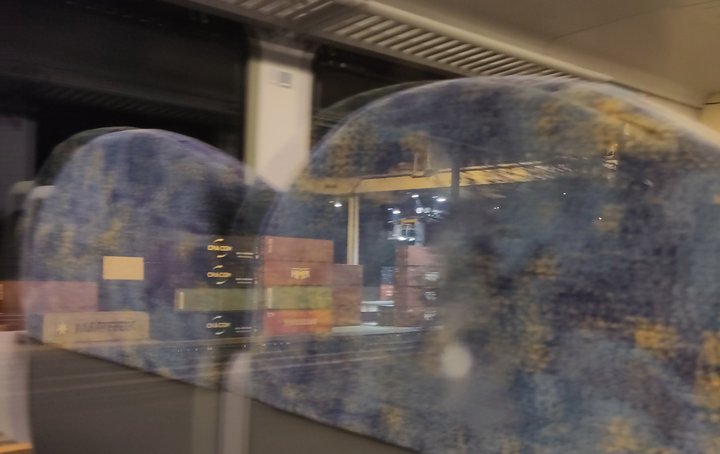Blick aus einem Zugfenster im dunkeln, im fenster spiegeln sich die sitze, draußen container